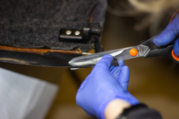 Tailor's hands in blue, rubber gloves while working with fabric.Tightening of the car interior.The hands of a girl in blue gloves while working with scissors with fabric selective focus.