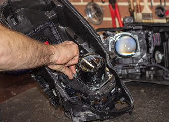 Fototapeta na wymiar Car headlight in repair close-up. The car mechanic installs the lens in the headlight housing. The concept of a car service.Installation of LED lenses in the headlight. LED lens.Restoration of optics.