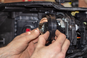 Car headlight in repair close-up. The car mechanic installs the lens in the headlight housing. The concept of a car service.Installation of LED lenses in the headlight. LED lens.Restoration of optics.