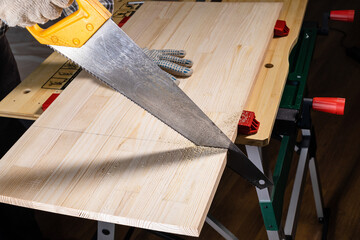 side view of sawing wooden board with hand saw on workbench at home