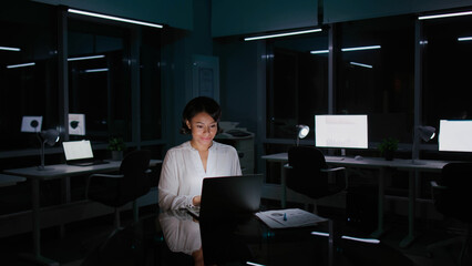 Portrait of African-American businesswoman typing on laptop and smiling working late in dark office