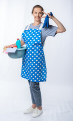 european housewife in a kitchen apron, jeans on a white background, full length portrait. a woman holds a basin with detergents and rubber gloves. cleaning company. cleanlines