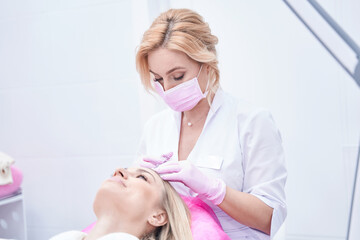 Concentrated female dermatologist performing hair mesotherapy procedure