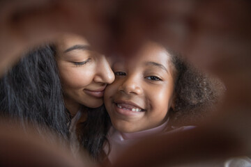 Cheerful Black mom and sweet little daughter kid with tooth gap making hand heart frame, joining fingers, looking at camera, showing symbol of love, gratitude, family, kindness. Close up