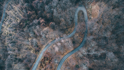 Aerial high angle view of narrow winding curvy mountain road among the trees in winter forest. Bird's eye view landscape.