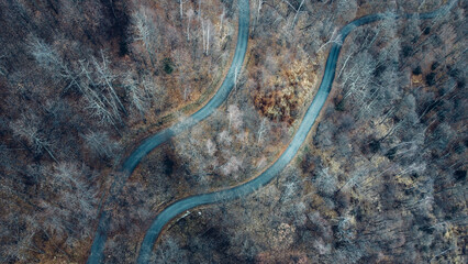Aerial high angle view of narrow winding curvy mountain road among the trees in winter forest. Bird's eye view landscape.