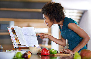 Following the recipe to the letter. A young woman cooking from a recipe book.