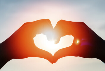 Love romance background concept. Hand heart shape with sunset sky with lover silhouette on the...