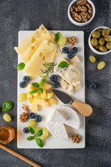 Cheese plate with a variety of cheeses, honey, grapes, nuts, olives, blueberries and fresh herbs on a concrete background. A festive snack.
