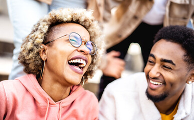 Multicultural couple on genuine laughter - Life style concept with happy multiracial friends having fun together out side - Trendy college students enjoying break time at campus - Warm vivid filter