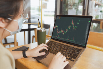 Asian Businesswoman, female trader, investor with medical face mask using laptop, tablet for stock market, Bitcoin cryptocurrency trading, money investing on online trading platform. Trading concept. - 495257034