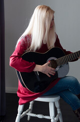 Fototapeta na wymiar beautiful young blonde woman in a red dress with a black guitar, favorite hobby