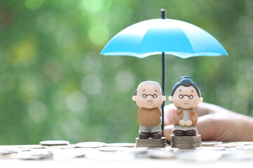 Mutual fund,Love couple senior and hand holding the umbrella with stack of coins money on natural green background, Save money for prepare in future and pension retirement concept - obrazy, fototapety, plakaty