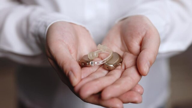 Close up of young woman holding hearing aid equipment. Woman holding hearing aid equipment on white background. The hearing aid lies in the female palm. Hearing aid concept