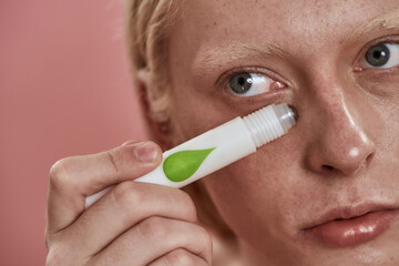 Guy applying depuffing eye serum on his face skin