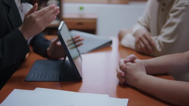 Happy young Asian financial planer professional advisor sitting talking and presenting financial retirement plan on tablet to the mature retirement couple in front the desk top at home office