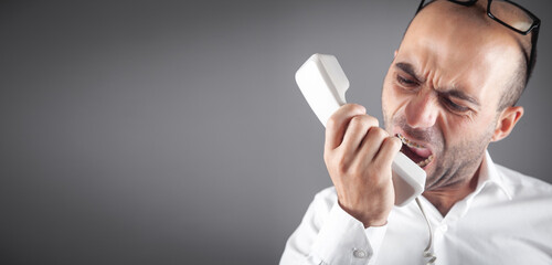 Caucasian angry businessman screams into the telephone receiver.