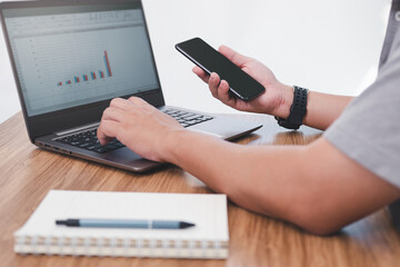 Close up hand a man hold smartphone check customer service statistics data of the car service center and use laptop notebook on table