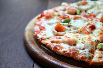 Hot seafood Italian pizza slice with melting cheese on wooden table.