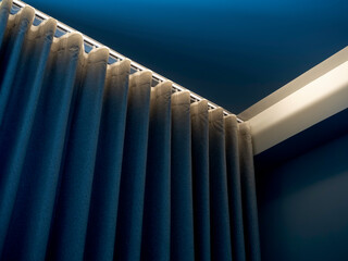 Close-up of blue wall curtain on curtain rail decorated with hidden light under the ceiling near...