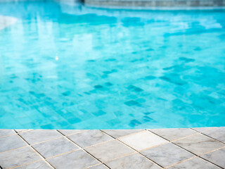 Summer pool background. Empty space on the pool edge, marble stone tiles and blurred swimming pool...