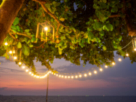 Abstract blurred of lamp and hanging light bulb bokeh on tree background on sunset, yellow string lights with bokeh decor in outdoor restaurant in the night party.
