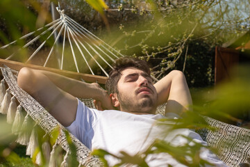 Jeune homme de 20 ans qui fait la sieste dans son jardin au soleil, allongé dans un hamac. Au...