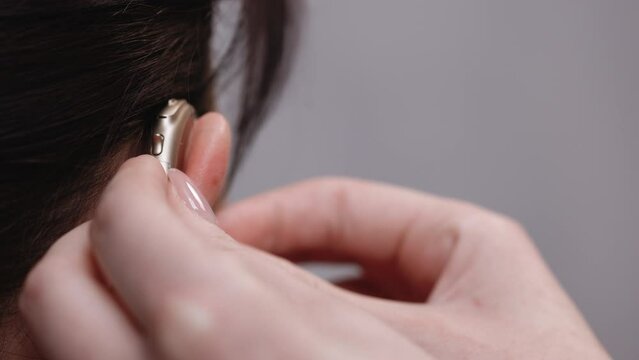 Woman with symptom of hearing loss. Female nurse wears a hearing aid. Mature tensed woman with fingers near ear. Woman with hearing aid.