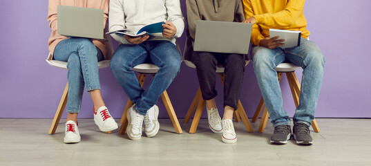 Diverse university students in casual jeans and sneakers sitting in row, preparing assignment for class, working on laptop computer devices, sharing academic course study notes. Low section legs, feet - Powered by Adobe