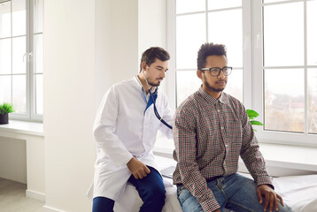 Young man during health checkup at doctor's office. Physician at modern clinic or hospital sitting...