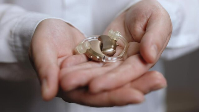 Close up of elderly woman holding hearing aid equipment. The hearing aid lies in the female palm. Hearing aid concept. Woman holding hearing aid equipment on white background