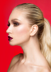 Beauty portrait of young model with makeup with bare shoulders, over red background.