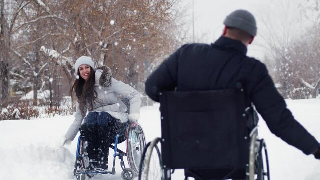 Disabled man and woman in wheelchairs play snowballs in winter at park having fun. Disabled couple is playing snowballs. Concept of relationships and fun