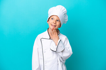 Little chef boy isolated on blue background looking up while smiling