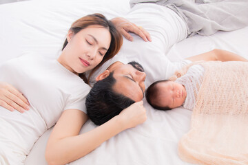 Obraz na płótnie Canvas Asian young mother father and newborn sleep on bed together. Parent take a nap with baby because tired nurturing baby. Little infant deeply sleeping wrapped in thin white cloth with happy and safe.