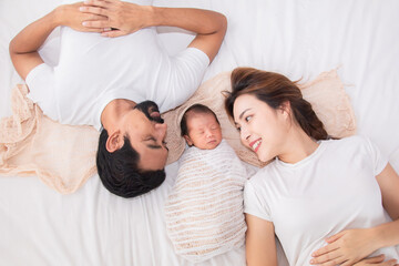 Asian young mother father and newborn lying on bed together. Mom and dad happy parents sleep next...