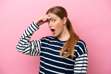 Young caucasian woman isolated on pink background doing surprise gesture while looking to the side