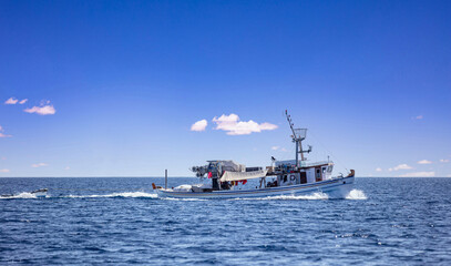 Fishing boat return. Trawler sails in Aegean rippled sea, blue sky background. Cyclades Greece.