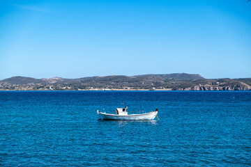 Milos Greek island, Cyclades. Fishing boat moored in open Aegean calm sea, blue sky background.
