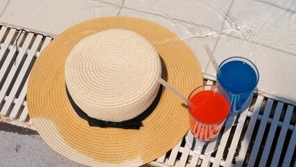 Fototapeta na wymiar Two colorful cocktail glasses pink and blue, sun hat on the edge of the swimming pool, close up. Vacation concept, hotel relaxation, all inclusive