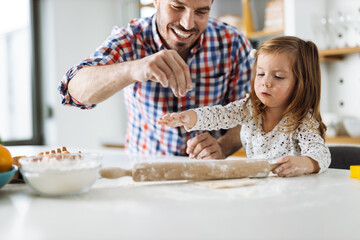 Cute girl and her father making cookies while baking in the kitchen