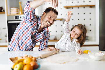Cute girl and her father making cookies while baking in the kitchen. Focus is on little girl