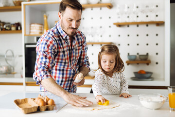 Cute girl and her father making cookies while baking in the kitchen