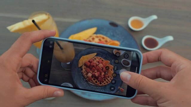 Female hands using smartphone to take photos of waffle with red fruits and mango