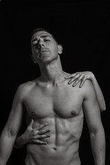 Fototapeta premium Black and white vertical image of a man with a naked torso and a woman's hands that grab him from behind. Close-up shot of female hands on a man's naked fitness body.