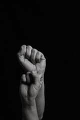 Vertical black and white image of two arms with clenched fists coming out from below. Close shot of a woman's and a man's arm with their fingers closed together leaving copy space.