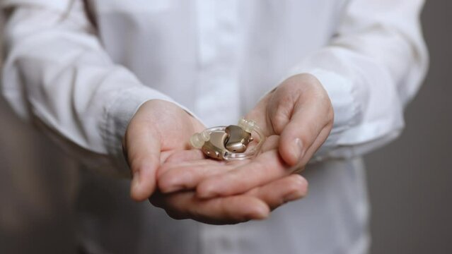 Close up of woman holding hearing aid equipment. The hearing aid lies in the female palm. Hearing aid concept. Woman holding hearing aid equipment