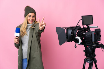 Reporter woman holding a microphone and reporting news over isolated pink background smiling and showing victory sign