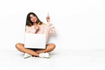 Naklejka premium Young woman with a laptop sitting on the floor isolated on white background pointing with the index finger a great idea