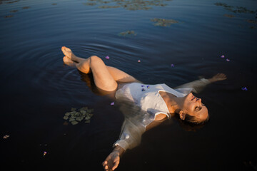 A beautiful slovenic girl in a white dress poses in a river with water lilies. The fairy tale of...
